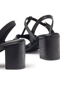 Black heeled sandals with a block heel, featuring crisscross straps and a smooth leather finish. Textured heel adds visual interest.