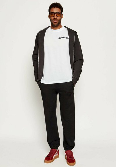 Felpa nera con zip, t-shirt bianca con logo, pantaloni della tuta neri e sneakers rosse con dettagli bianchi. Texture del tessuto liscia in tutto.