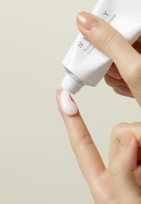 Una crema blanca se está dispensando de un tubo sobre la yema de un dedo. La crema tiene una textura suave y brillante, y es ligeramente espesa.