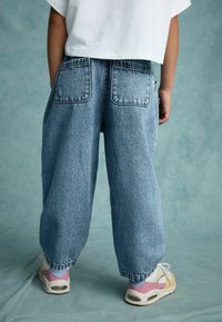 Ljusblå, löst sittande denimbyxor med två bakfickor och strukturerad yta, kombinerade med vita och pastellfärgade sneakers.
