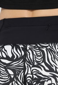 Leggings bianchi e nere con un motivo a strisce zebrate, realizzati in tessuto liscio, dotati di una tasca nascosta e dettagli di cucitura a contrasto.