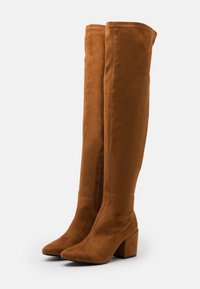 Botas marrones de ante por encima de la rodilla con punta afilada, tacón cuadrado y cremallera lateral. Textura suave y diseño elegante.