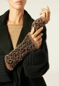 Braun gefleckte Faux-Fur-Armwärmer mit gestrickten schwarzen Bündchen, getragen über einem beigen Pullover und einem schwarzen Mantel, die Textur und Muster hervorheben.