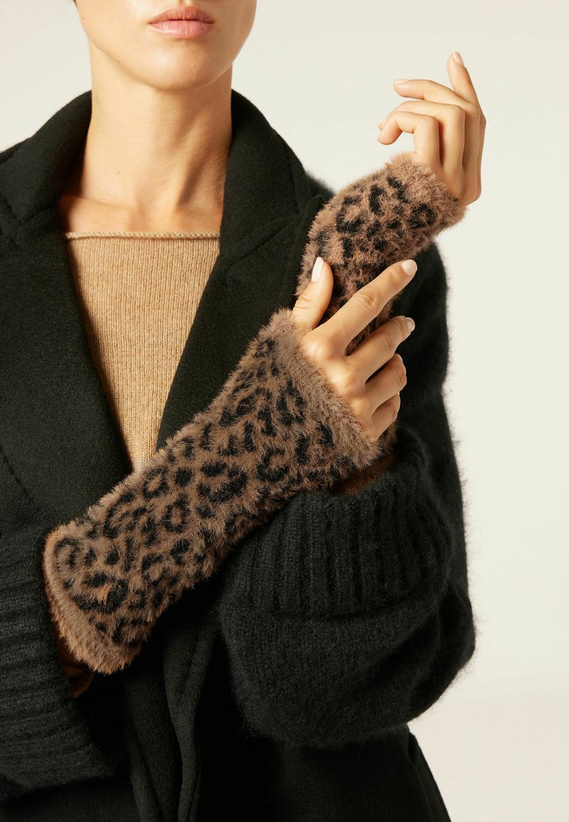 Braun gefleckte Faux-Fur-Armwärmer mit gestrickten schwarzen Bündchen, getragen über einem beigen Pullover und einem schwarzen Mantel, die Textur und Muster hervorheben.