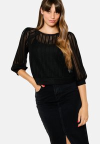Maglione nero lavorato a maglia con un design testurizzato, maniche a tre quarti e orlo corto, abbinato a una gonna nera a vita alta.