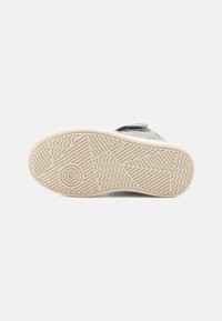 La suela de un zapato muestra un material de goma texturizado en color crema, con estrías y patrones circulares para mejorar la tracción.