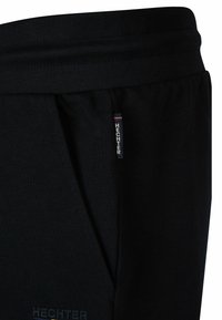 Zwarte sport shorts gemaakt van zachte stof, met een elastische tailleband, zijzakken en een klein merklabel met rode en blauwe accenten.