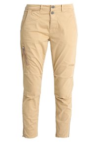 Beżowe spodnie slim fit z podwójnym zapięciem w talii, ukośnymi kieszeniami z przodu, zamkniętą kieszenią na lewym udzie oraz zamkami błyskawicznymi na mankietach.