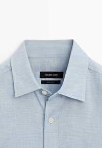 Camicia in lino azzurro chiaro con colletto classico, chiusura con bottoni bianchi e etichetta con la scritta "Massimo Dutti, Made in Turkey".