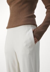 Haut marron à manches longues côtelé avec des manches ajustées, assorti à un pantalon blanc à jambes larges, doté de poches latérales et d'une texture lisse.
