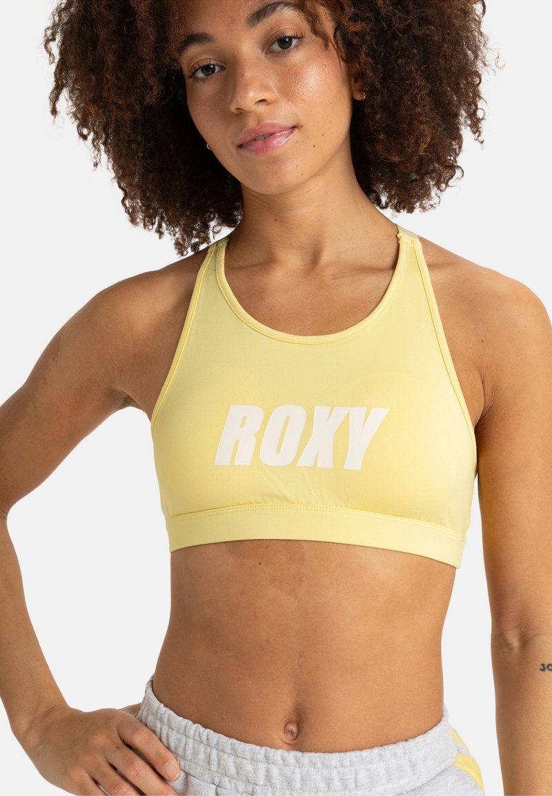 Žltá športová podprsenka s bielym logom "ROXY". Vyrobená z hladkej látky, s pretekárskym strihom a podporným pásom pod prsiami.