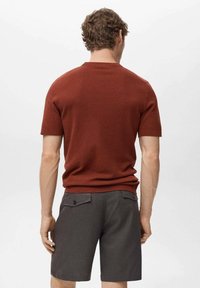 Korte mouwen, roestkleurige gebreide trui met een gestructureerde afwerking, gecombineerd met grijze shorts met achterzakken en knoopdetails.