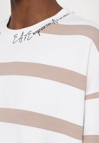 Hvit hettegenser med brede beige horisontale striper og brodert "EA7 Emporio Armani" på halsen. Mykt bomullstoff.