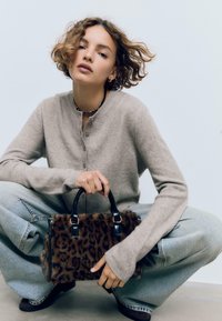 Borsa a tracolla con stampa leopardata, manici in pelle nera, texture morbida e hardware in argento, abbinata a un cardigan beige e jeans in denim chiaro.