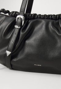 Schwarze Lederhandtasche mit gerafftem Design, verstellbarem Schulterriemen, silbernen Hardware-Details und einem dezenten Logo an der Seite.