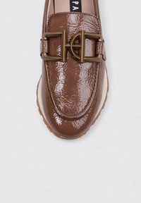 Mocasín de charol marrón con punta redondeada, detalle prominente de hebilla en tono dorado y suela de goma blanca. Textura lisa y brillante.