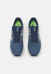 Baskets de sport bleu marine avec un upper en tissu texturé, des accents blancs et une semelle intérieure verte. Présente des lacets et un design de bout arrondi.