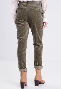 Olijfkleurige corduroy broek met rechte pijpen, opgerolde manchetten en achterzakken. G gedragen met lichtbruine enkellaarsjes met een blokhak.