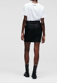 White short-sleeve t-shirt paired with a fitted black sequin mini skirt and black ankle boots, showcasing shiny texture and fitted silhouette.
