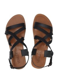 Schwarze flache Sandalen mit überkreuzten Riemen, braunem Lederfußbett, verstellbarem Knöchelriemen und abgesteppten Details auf dem Fußbett.