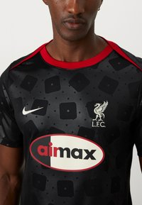 Camiseta de fútbol negra con acentos rojos, con un patrón geométrico, logo de Nike, emblema de LFC y un gráfico central "aimax".