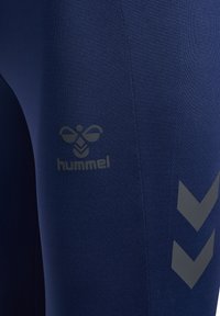 Leggings elásticos de color azul marino con un logotipo gris mate y un patrón de chevrón en el costado. El material parece suave y ajustado al cuerpo.