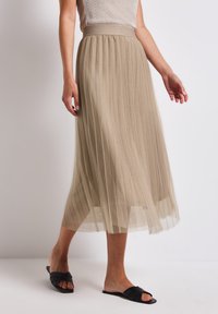 Pleated midi-hame vaaleassa beigessä, valmistettu läpinäkyvästä kankaasta. Ominaisuuksiin kuuluu teksturoidut vyötärö ja virtaava muotoilu, sekä mustat liukusandaalit.