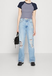 Světle modré džíny z denimu s širokým střihem a roztržením na stehnech, v kombinaci s přiléhavým šedým a námořnickým cropped tričkem a černou taškou.