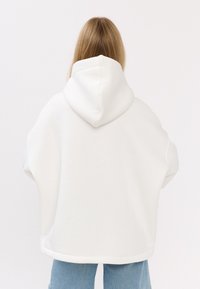 Witte hoodie met een ontspannen pasvorm, met een zachte textuur en een naad aan de onderzijde, gecombineerd met lichtblauwe spijkerbroek.