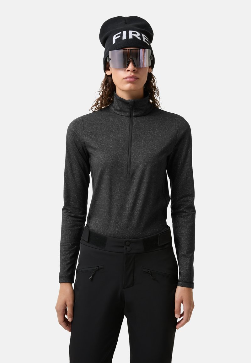 Sort langærmet top med lynlåshals, lavet af tekstureret, glitrende stof. Kombineret med sorte bukser med lynlåslommer og bred taljebånd.