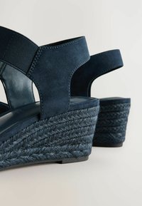 Marine wedge sandaler med blødt ruskindsoverdel, elastiske stropper og flettet jute hæl, samt en struktureret, gummiagtig sål for bedre greb.