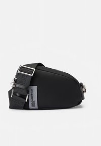 Mala de ombro em nylon preto com uma forma elegante e curva. Apresenta uma fivela metálica prateada, alça ajustável e detalhes do logótipo na frente.