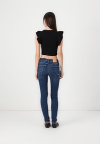 Black cropped top with ruffled sleeves paired with fitted blue jeans. The jeans feature a small back pocket and a tan rectangular label.