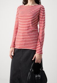 Rød og beige stribet langærmet top parret med en sort denimnederdel, holder en sort håndtaske med sølvhardware accenter.