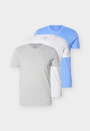 Trois t-shirts à col rond pliés empilés, gris devant, blanc au milieu et bleu clair derrière, sur un fond clair uni.