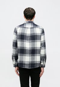 Koszula w kratę w kolorach granatowym, białym i szarym. Posiada długie rękawy i kołnierzyk. Materiał ma miękkie, lekko teksturowane wykończenie. Widoczne mankiety na guziki.