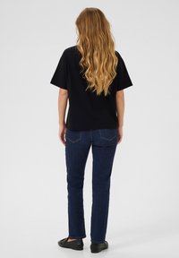 Black short-sleeve top paired with dark blue denim jeans. The jeans feature a simple back pocket design with subtle stitching.
