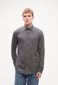 Grå långärmad skjorta med krage, med svarta knappar och ett mjukt, strukturerat tyg. Buren med blå jeans.