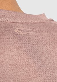 Camiseta deportiva color rosa con una tela texturada. Presenta un pequeño logo tonal en el cuello. Cuello redondo y mangas cortas.