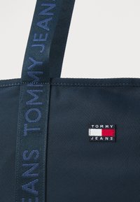 Geantă de umăr de culoare bleumarin, cu textură din material și patch brodat cu logo. Dispune de o curea lungă cu textul "TOMMY JEANS". Design simplu și funcțional.