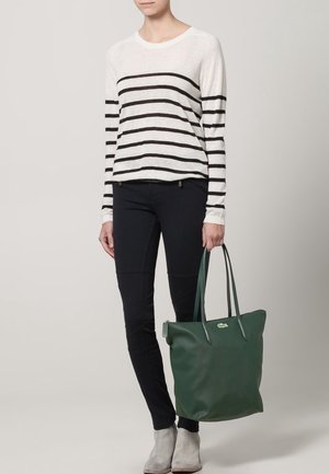 Chemise à manches longues rayée, noire et blanche ; pantalon noir cintré ; sac fourre-tout en cuir vert avec double poignée ; bottines grises.