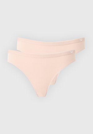 Dva svetlo béžové bezšvové dámske tangá s malým logom na páse na jednofarebnom pozadí.