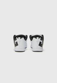 Zapatillas bajas blancas y negras con parte superior de cuero liso, talón negro en contraste y un gran logo negro en el lado exterior.