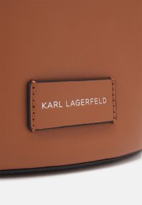 Surface en cuir marron avec une étiquette rectangulaire cousue affichant le texte "KARL LAGERFELD" en lettres blanches majuscules.
