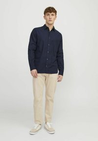 Marineblå skjorte med lange ærmer, en klassisk krave og brune knapper, parret med beige bukser og lyse sneakers.