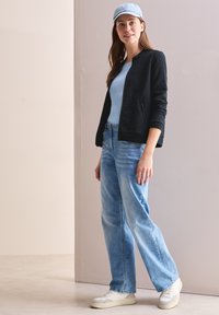 Chaqueta bomber negra con cremallera, camiseta de color azul claro, jeans holgados de denim claro y zapatillas blancas. La gorra es de color azul claro. Un atuendo simple y casual.