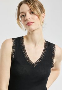 Débardeur noir à côtes avec un col en V et une dentelle sur les épaules. Texture douce, design ajusté.