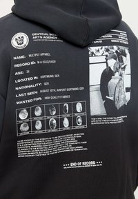 Sweat à capuche noir avec des éléments graphiques incluant du texte et une empreinte digitale au dos. Présente une conception structurée et une texture de tissu douce.