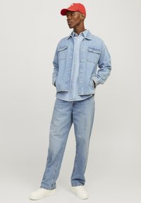 Lichtblauwe spijkerjack over een bijpassend shirt, met vier zakken. Combineert met blauwe spijkerbroek en witte sneakers. Rode pet maakt de outfit af.