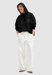 Felpa nera con cappuccio e grande stampa "ALLSAINTS LONDON", abbinata a pantaloni cargo bianchi con tasche utili e gambe larghe.